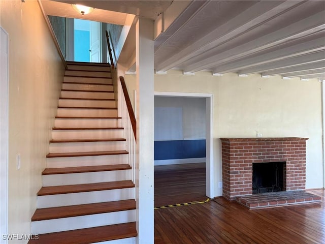 stairs featuring beam ceiling, hardwood / wood-style floors, and a brick fireplace