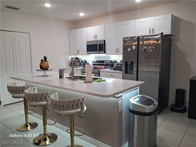 kitchen featuring stainless steel appliances, white cabinetry, a kitchen island with sink, and a breakfast bar area