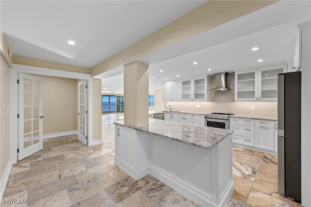 kitchen featuring appliances with stainless steel finishes, white cabinetry, decorative backsplash, light stone countertops, and wall chimney exhaust hood