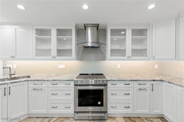 kitchen with stainless steel range with electric stovetop, wall chimney exhaust hood, sink, and white cabinets