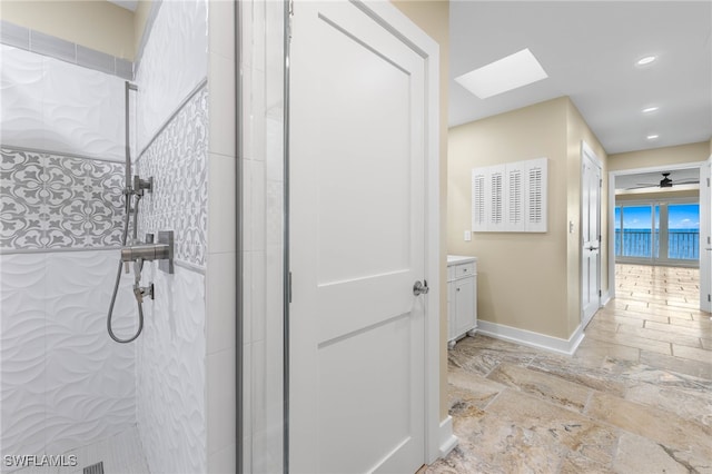 bathroom with vanity, a tile shower, ceiling fan, and a skylight