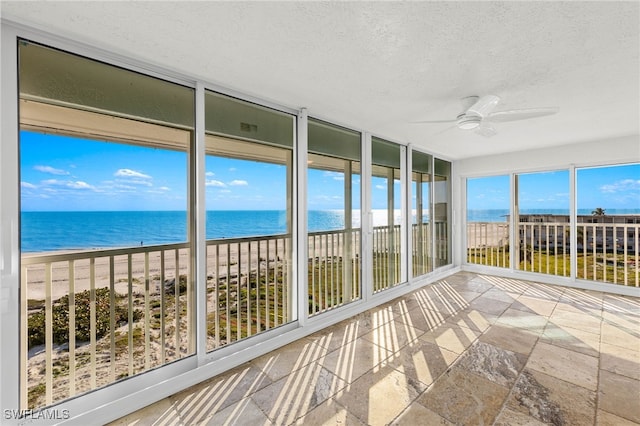 unfurnished sunroom featuring ceiling fan, a beach view, and a water view