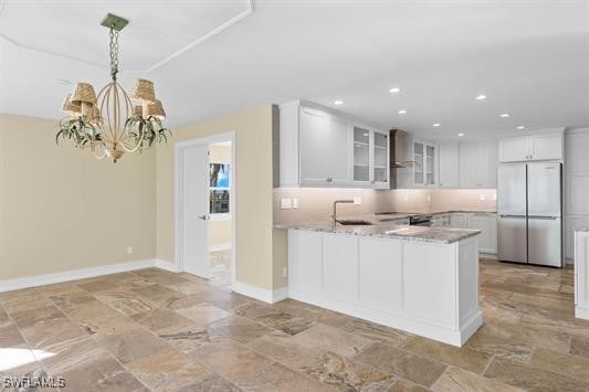 kitchen with white cabinetry, sink, stainless steel fridge, kitchen peninsula, and light stone countertops