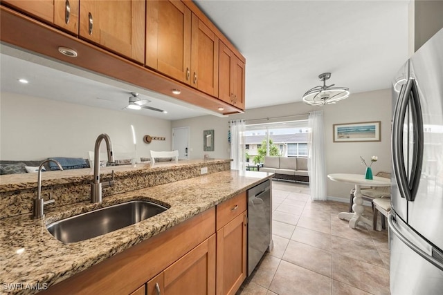 kitchen with light tile patterned flooring, appliances with stainless steel finishes, sink, ceiling fan, and light stone countertops