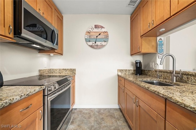 kitchen featuring light stone counters, sink, light tile patterned floors, and stainless steel appliances