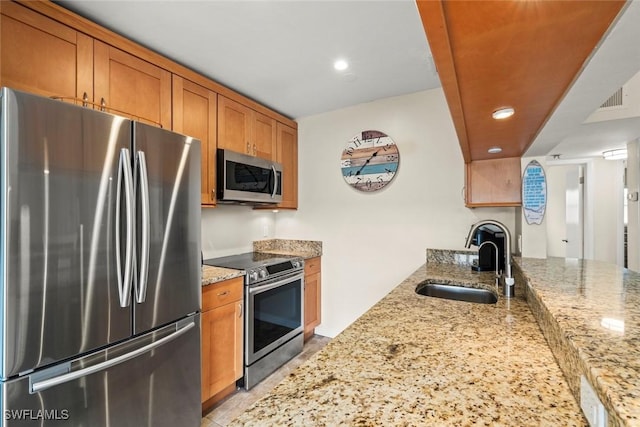 kitchen with stainless steel appliances, light stone countertops, sink, and kitchen peninsula