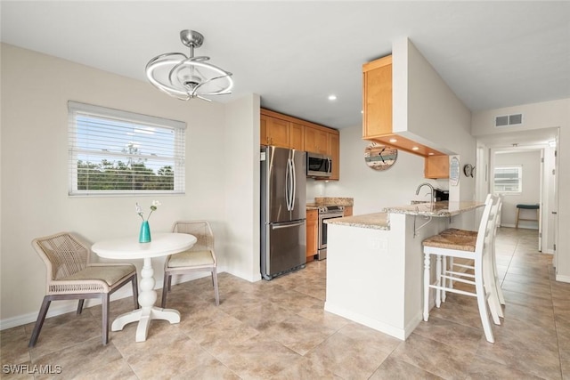 kitchen featuring sink, appliances with stainless steel finishes, a kitchen breakfast bar, kitchen peninsula, and light stone countertops