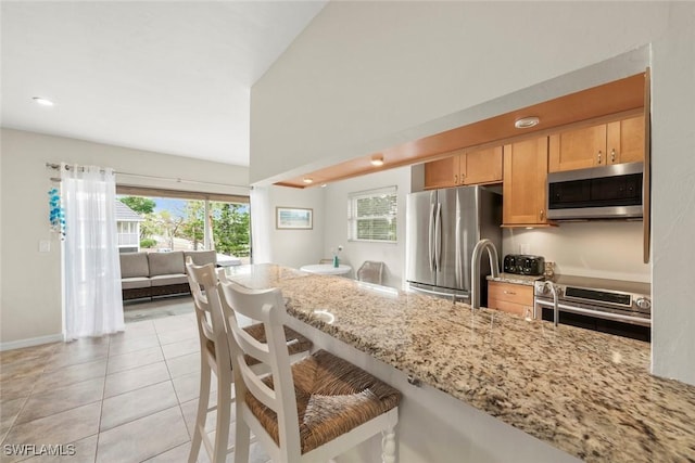 kitchen with light tile patterned floors, sink, appliances with stainless steel finishes, light stone counters, and a kitchen bar