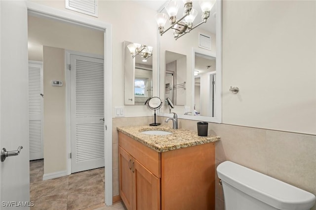 bathroom with tile patterned flooring, tile walls, an inviting chandelier, vanity, and toilet