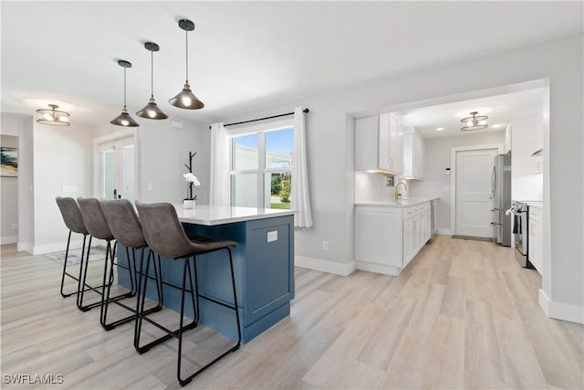 kitchen with decorative light fixtures, sink, white cabinets, stainless steel appliances, and light wood-type flooring