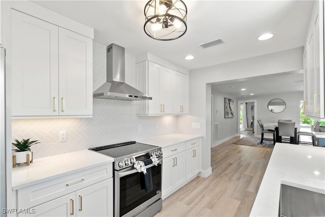 kitchen featuring white cabinetry, stainless steel electric range oven, light wood-type flooring, wall chimney range hood, and backsplash