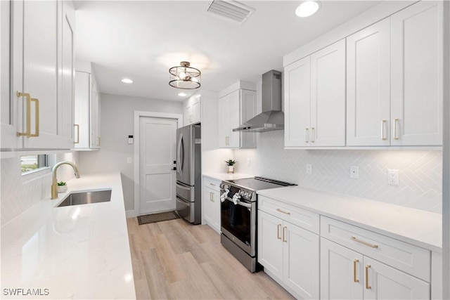 kitchen featuring appliances with stainless steel finishes, white cabinetry, sink, wall chimney exhaust hood, and light hardwood / wood-style flooring