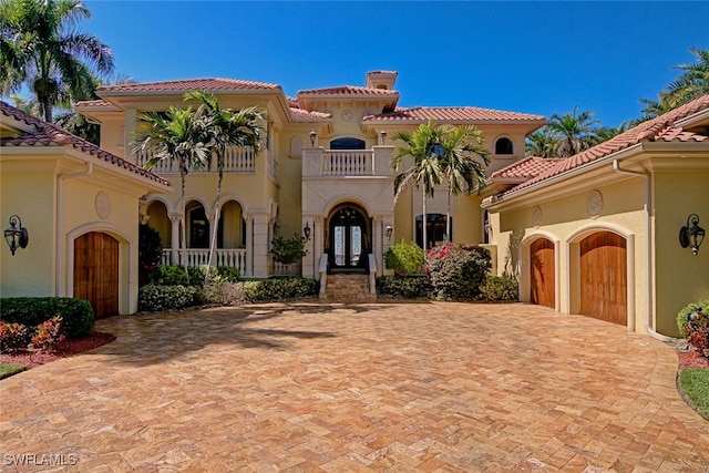 mediterranean / spanish house with decorative driveway, stucco siding, an attached garage, a balcony, and a tiled roof