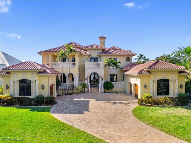 mediterranean / spanish-style home featuring a front yard, decorative driveway, a tile roof, and a balcony