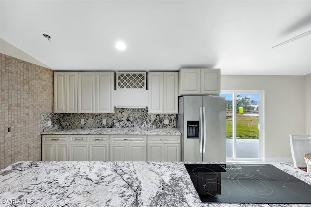 kitchen with decorative backsplash, stainless steel fridge, black electric cooktop, and lofted ceiling