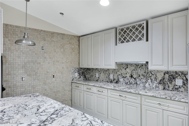 kitchen with vaulted ceiling, hanging light fixtures, decorative backsplash, and light stone counters