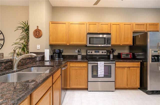 kitchen with sink, ceiling fan, dark stone countertops, stainless steel appliances, and light tile patterned flooring