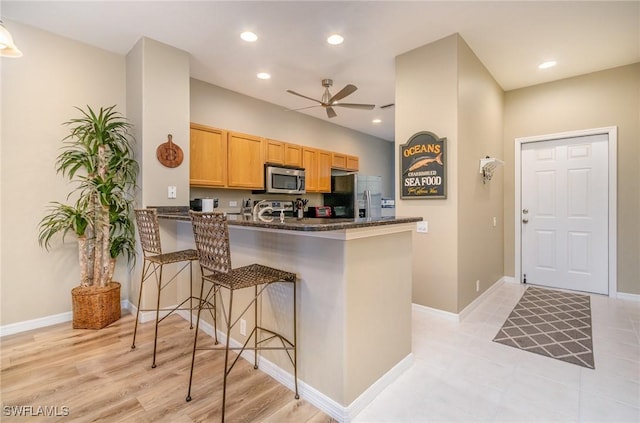 kitchen with appliances with stainless steel finishes, dark stone countertops, a kitchen breakfast bar, ceiling fan, and kitchen peninsula