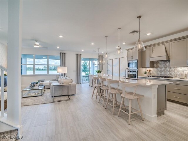 kitchen with gray cabinets, a kitchen island with sink, custom range hood, and appliances with stainless steel finishes