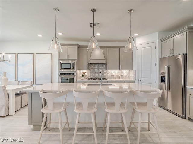 kitchen with stainless steel appliances, decorative light fixtures, a center island with sink, and gray cabinets