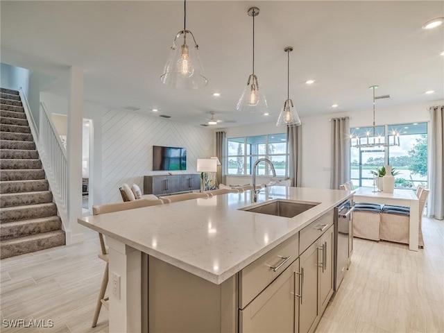 kitchen with light stone counters, sink, decorative light fixtures, and a kitchen island with sink