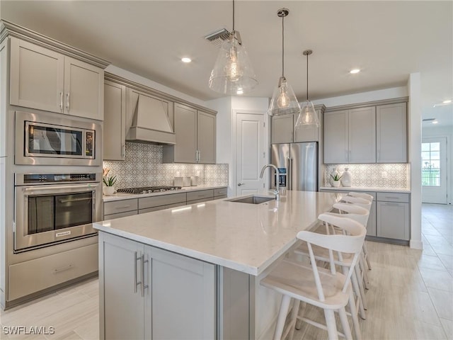 kitchen featuring pendant lighting, appliances with stainless steel finishes, sink, a kitchen island with sink, and custom range hood