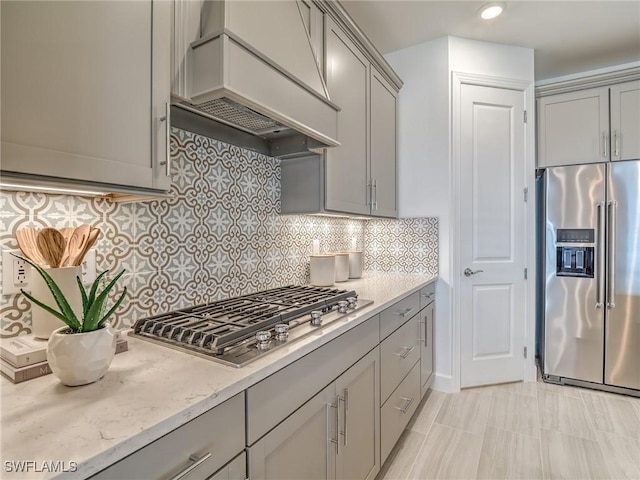 kitchen with stainless steel appliances, custom exhaust hood, gray cabinetry, and decorative backsplash