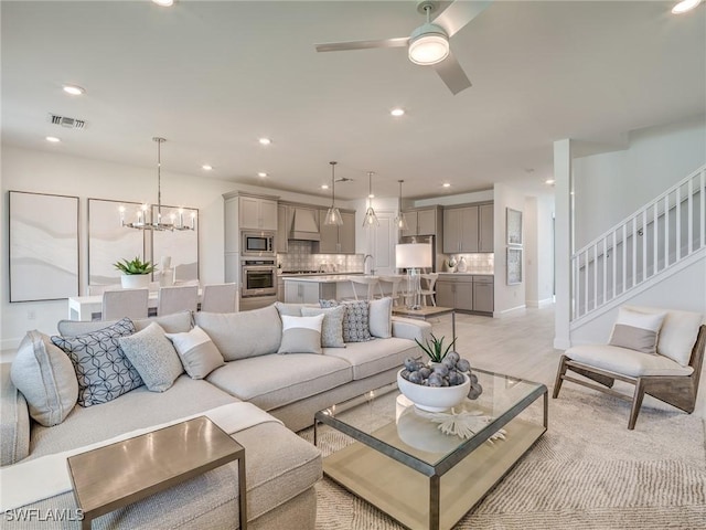 living room featuring ceiling fan with notable chandelier and light wood-type flooring