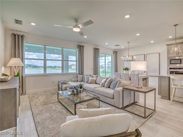 living room with ceiling fan with notable chandelier, a water view, a wealth of natural light, and light hardwood / wood-style floors