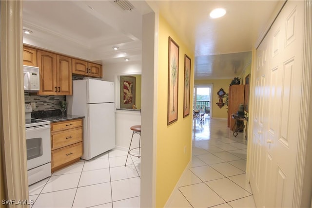 kitchen with dark stone counters, white appliances, light tile patterned floors, and decorative backsplash