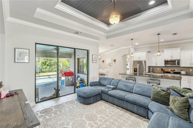 living room featuring crown molding, a tray ceiling, sink, and light tile patterned floors