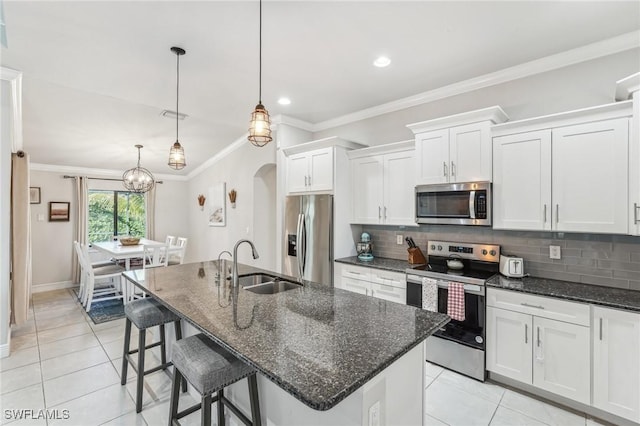 kitchen with appliances with stainless steel finishes, white cabinetry, sink, hanging light fixtures, and a center island with sink