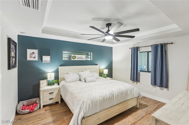 bedroom featuring wood-type flooring, ornamental molding, ceiling fan, and a tray ceiling