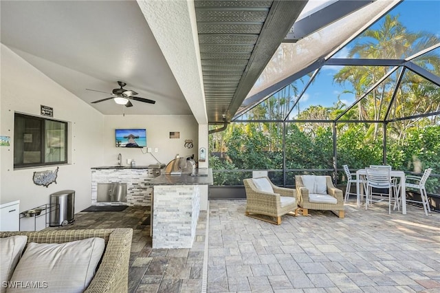 view of patio featuring sink, exterior kitchen, ceiling fan, and glass enclosure