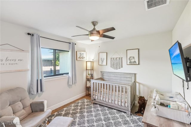 bedroom featuring a crib, wood-type flooring, and ceiling fan