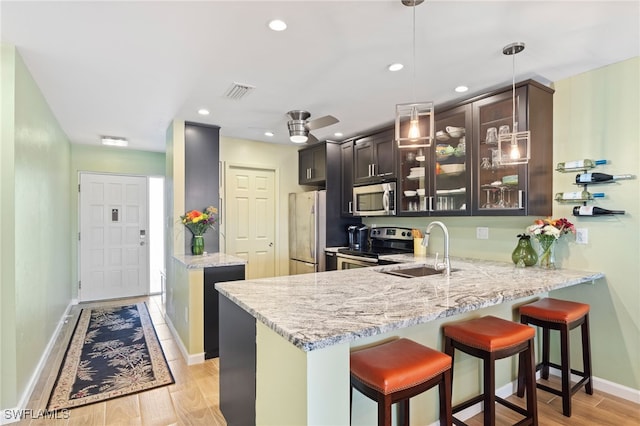 kitchen with kitchen peninsula, sink, light hardwood / wood-style floors, dark brown cabinetry, and stainless steel appliances