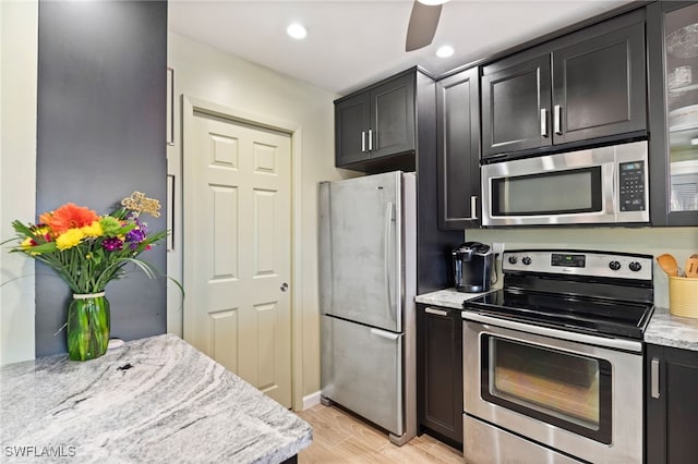 kitchen with ceiling fan, appliances with stainless steel finishes, light stone counters, and light hardwood / wood-style flooring