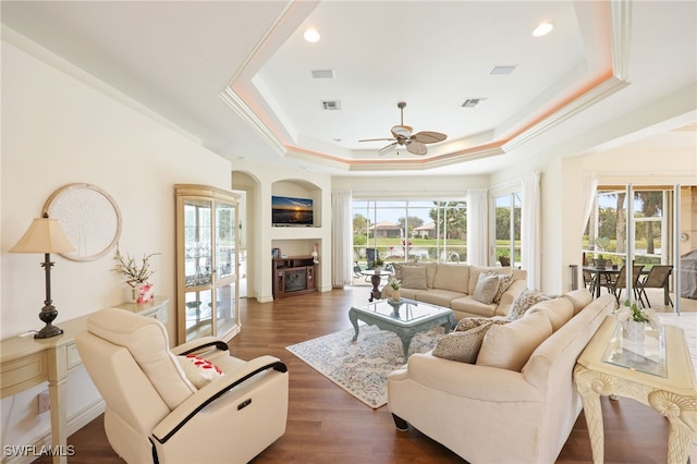 living room featuring crown molding, a fireplace, ceiling fan, dark hardwood / wood-style floors, and a tray ceiling