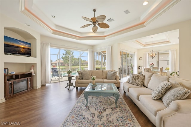 living room with ceiling fan with notable chandelier, a raised ceiling, crown molding, and dark hardwood / wood-style floors