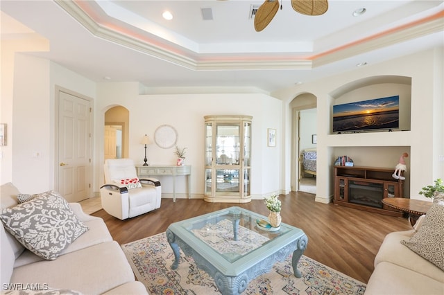 living room with a fireplace, ceiling fan, ornamental molding, hardwood / wood-style flooring, and a tray ceiling