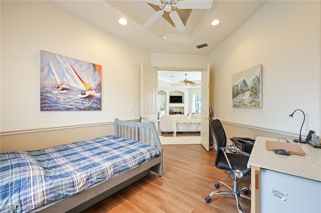 bedroom with wood-type flooring, a tray ceiling, and ceiling fan