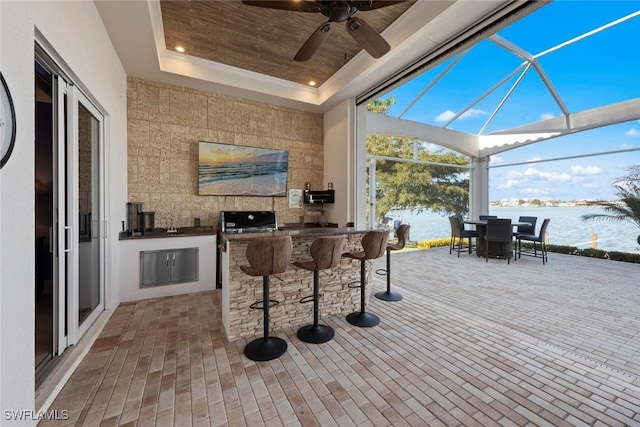 view of patio / terrace with a water view, a lanai, a bar, a grill, and exterior kitchen