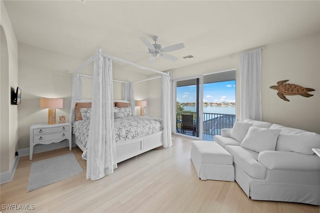 bedroom with access to exterior, light hardwood / wood-style flooring, ceiling fan, and a water view