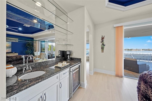 kitchen with sink, dark stone countertops, white cabinets, wine cooler, and a water view