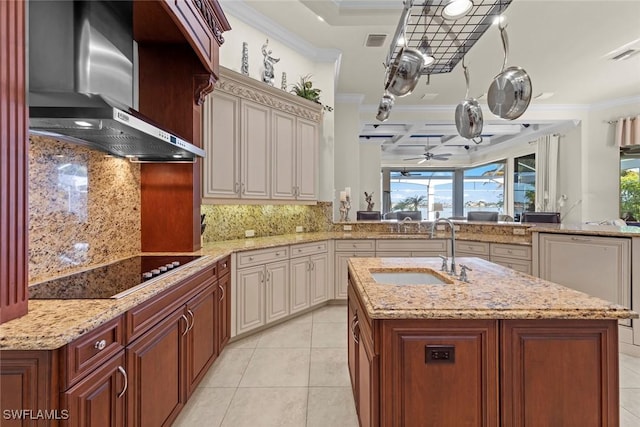 kitchen with an island with sink, sink, black electric stovetop, crown molding, and wall chimney exhaust hood