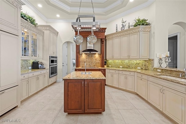 kitchen with sink, light stone counters, kitchen peninsula, a raised ceiling, and a center island with sink