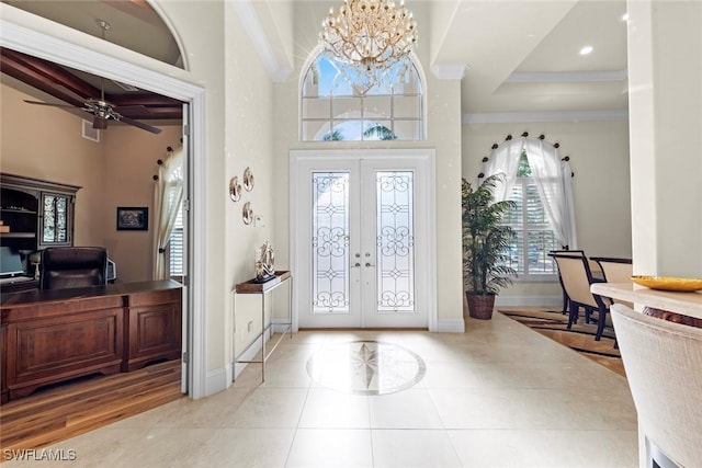 entryway with a towering ceiling, ceiling fan with notable chandelier, ornamental molding, light tile patterned floors, and french doors