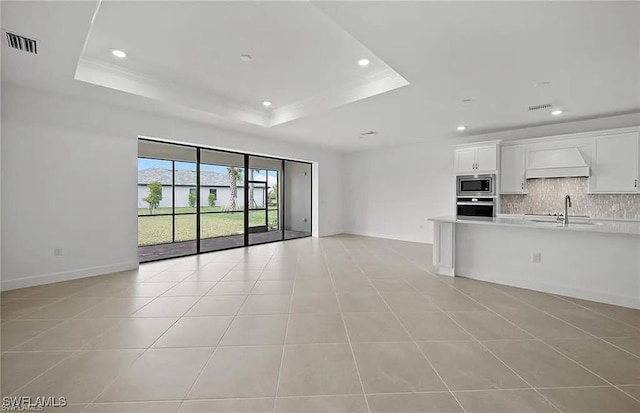 unfurnished living room with sink, a tray ceiling, and light tile patterned flooring