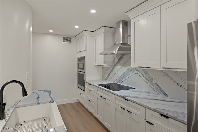 kitchen featuring appliances with stainless steel finishes, sink, wall chimney range hood, and white cabinets