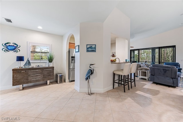 interior space with stainless steel fridge with ice dispenser, light tile patterned floors, a kitchen breakfast bar, and kitchen peninsula